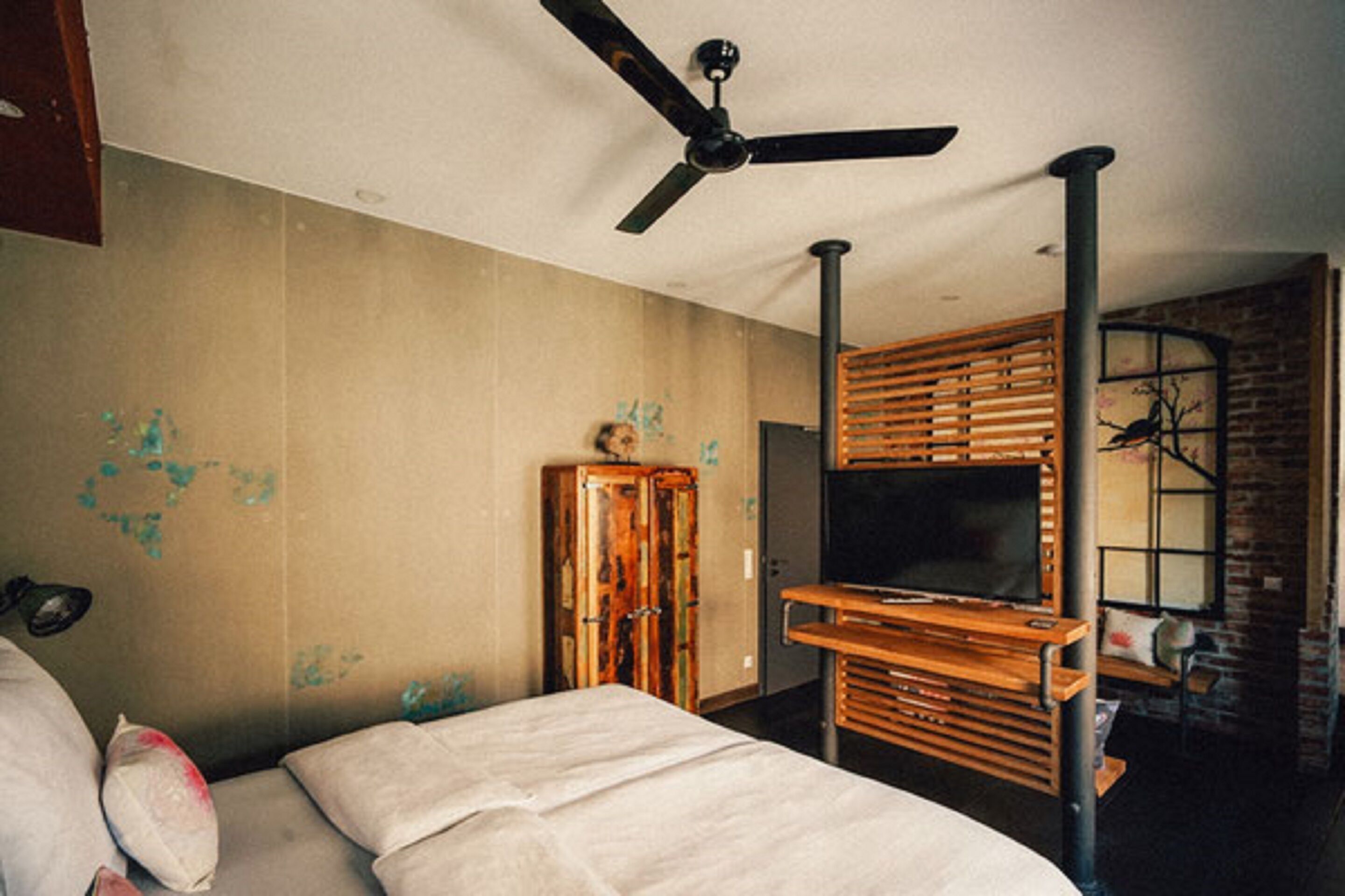 A room with a bed, a ceiling fan, a wooden cabinet, and a TV on a wooden stand.