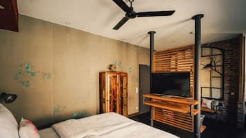 A room with a bed, a ceiling fan, a wooden cabinet, and a TV on a wooden stand.