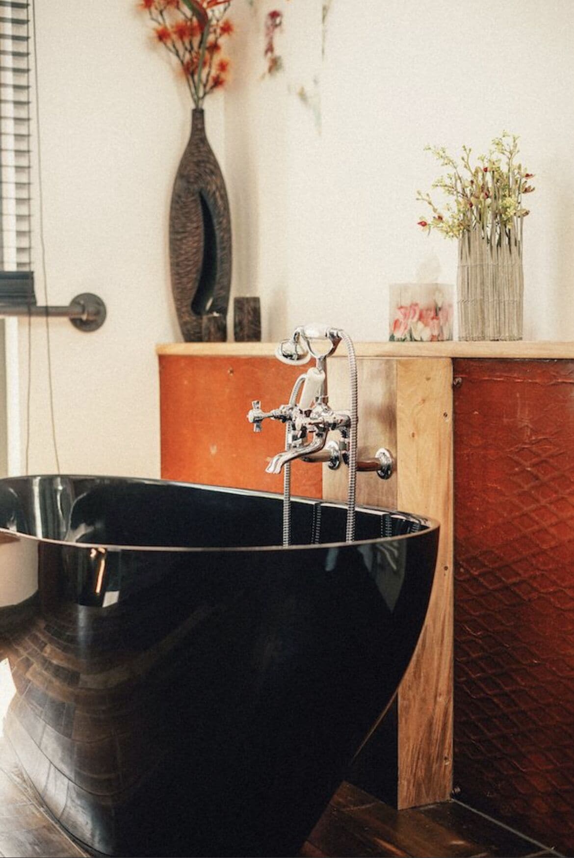 A black bathtub with a vintage faucet, a wooden cabinet, and a vase with flowers on top.