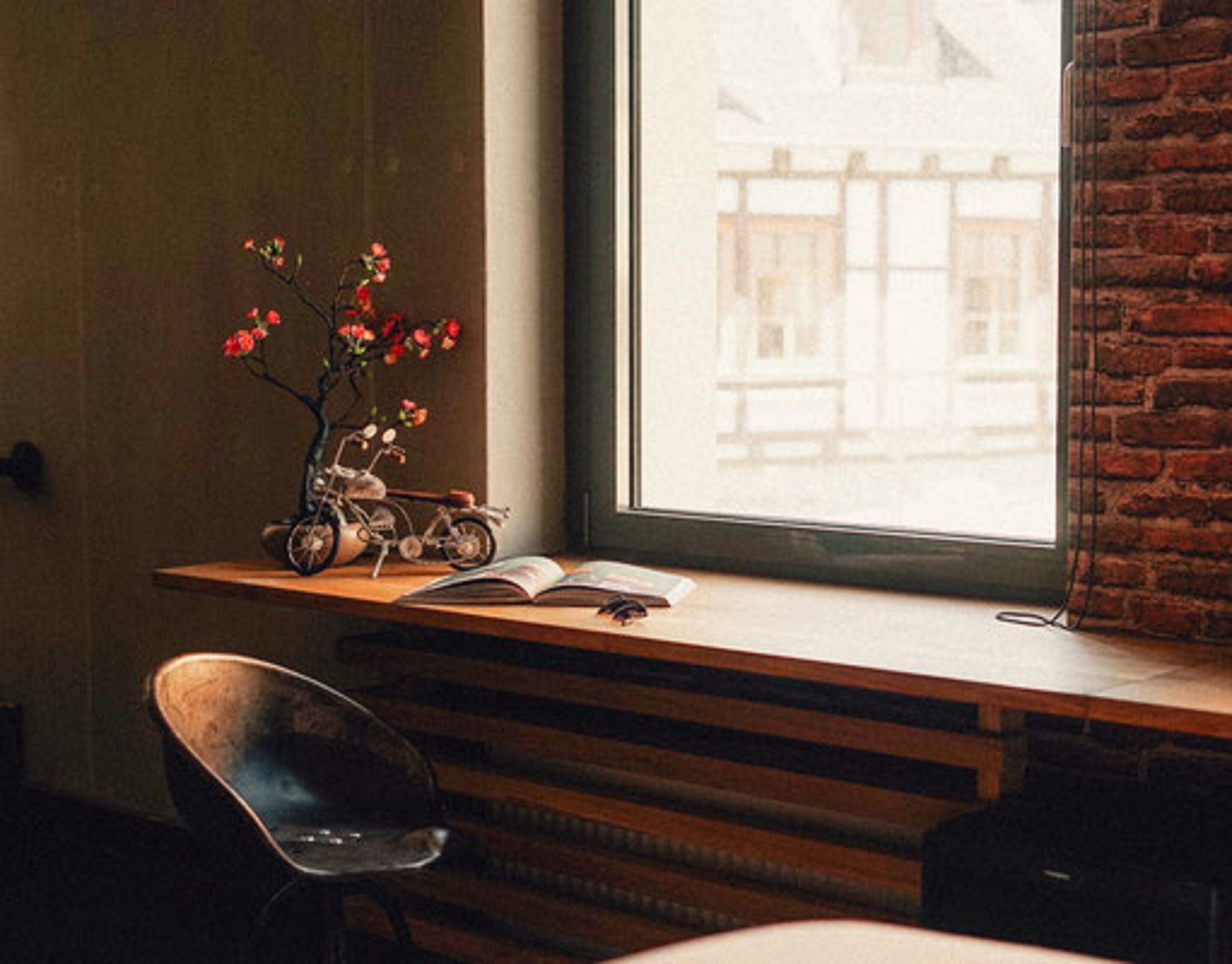 Una habitación con un escritorio de madera, una bicicleta, un florero con flores y una silla.