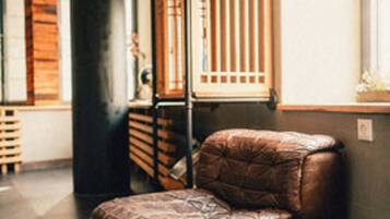 A brown leather chair in a room with a large black column, wooden slats, and a window with blinds.