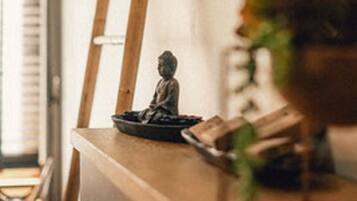 Ein Holztisch mit einer kleinen Statue, eine an der Wand angelehnte Leiter und eine Pflanze in einer Vase.