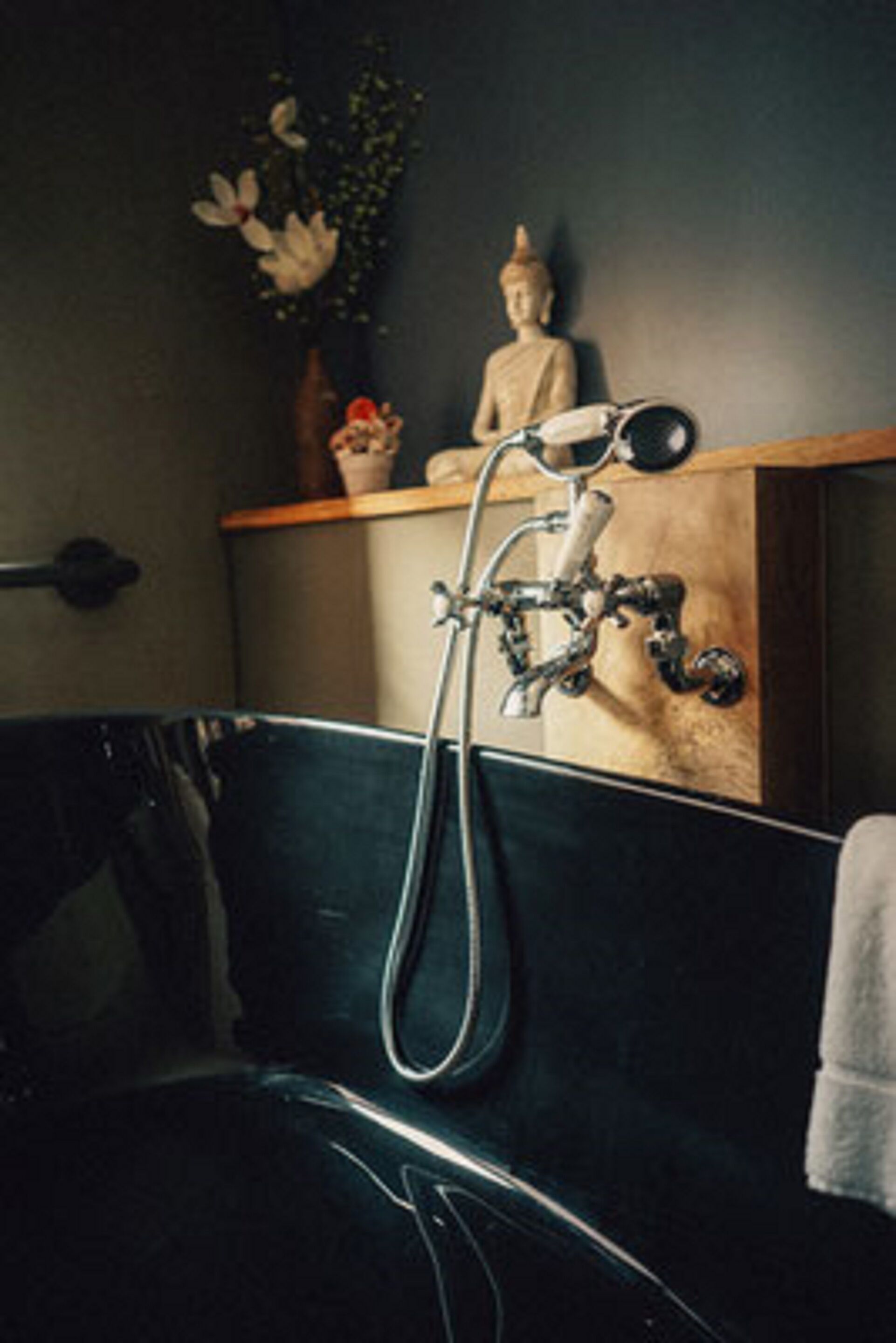 A bathroom with a black bathtub, a shower with a vintage faucet, a Buddha statue, and a small plant on the shelf.
