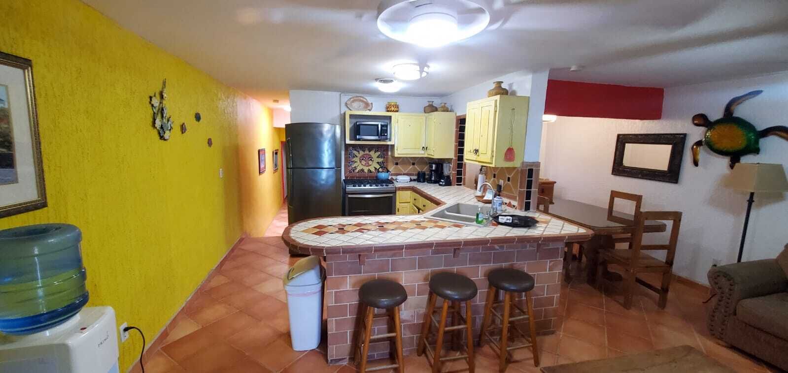 A compact kitchen with a central island, yellow walls, and a tiled backsplash.