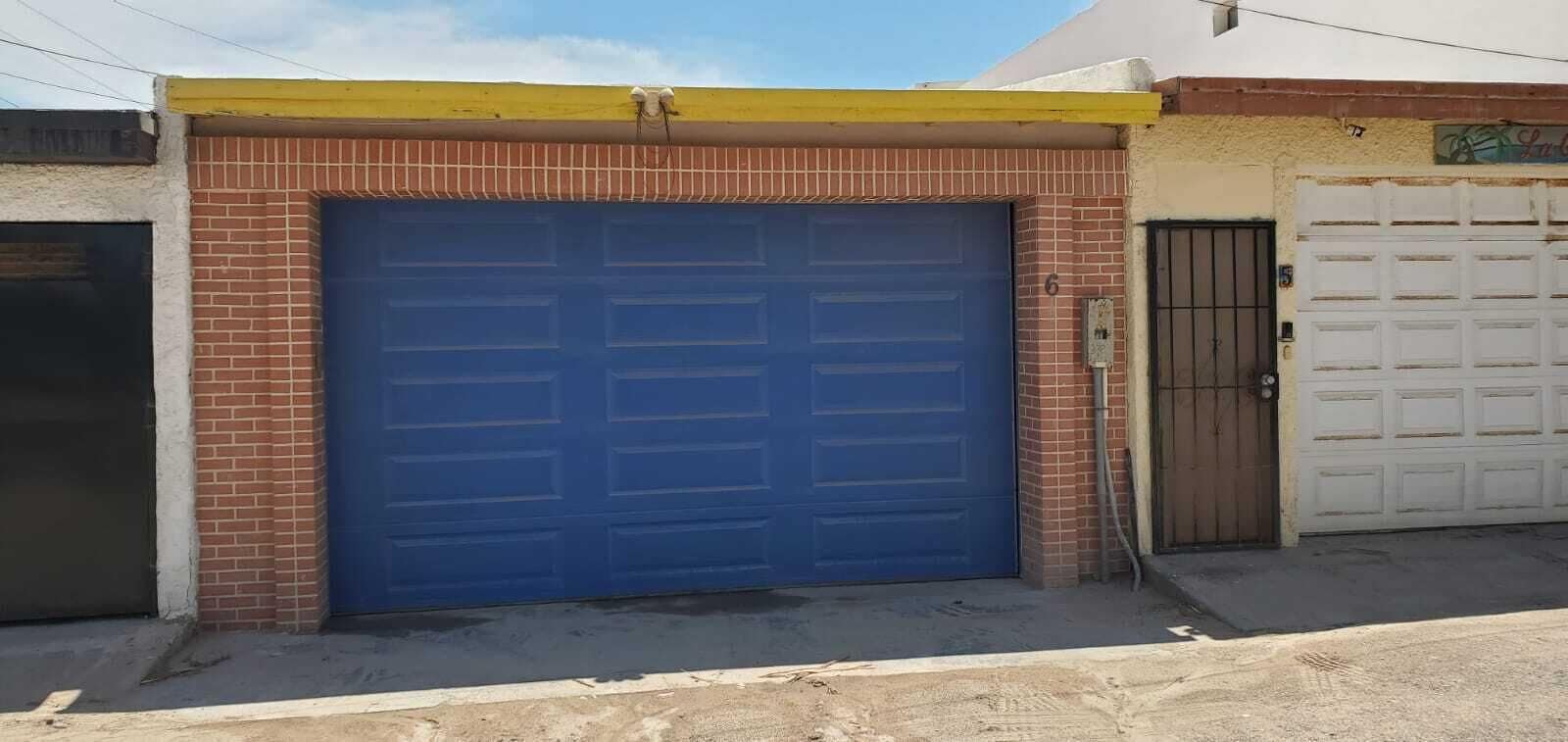 Un bâtiment doté d’un grand portail de garage bleu, d’une façade en briques et d’un toit jaune.