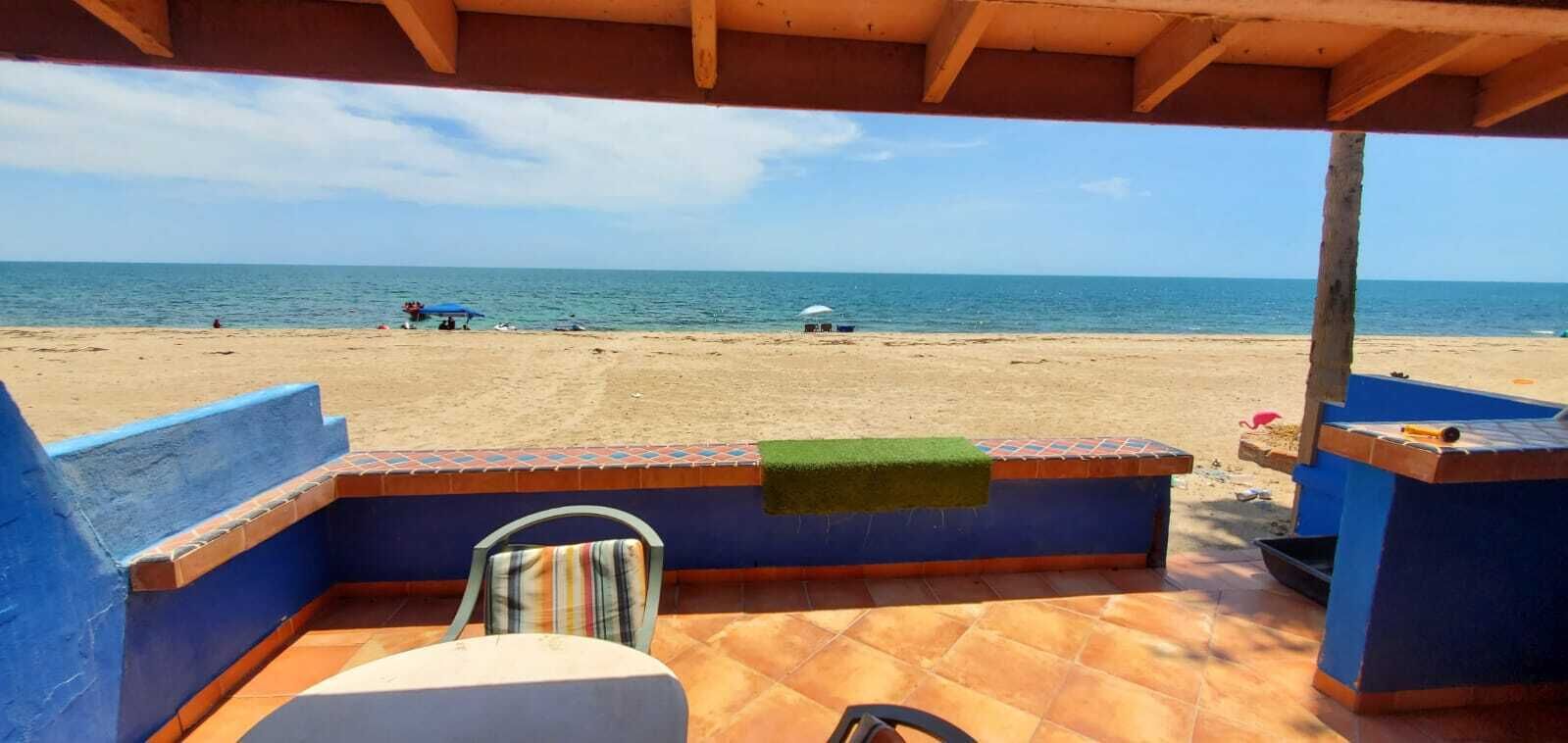 Une vue sur la plage depuis un patio abrité, avec une chaise et une table, donnant sur la mer.