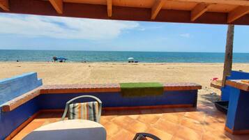 Une vue sur la plage depuis un patio abrité, avec une chaise et une table, donnant sur la mer.
