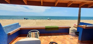 A beach view from a covered patio with a chair and a table, overlooking the sea. - Mirador Beach Escape: Direct Beachfront 3-Bedroom Home (Puerto Peñasco)