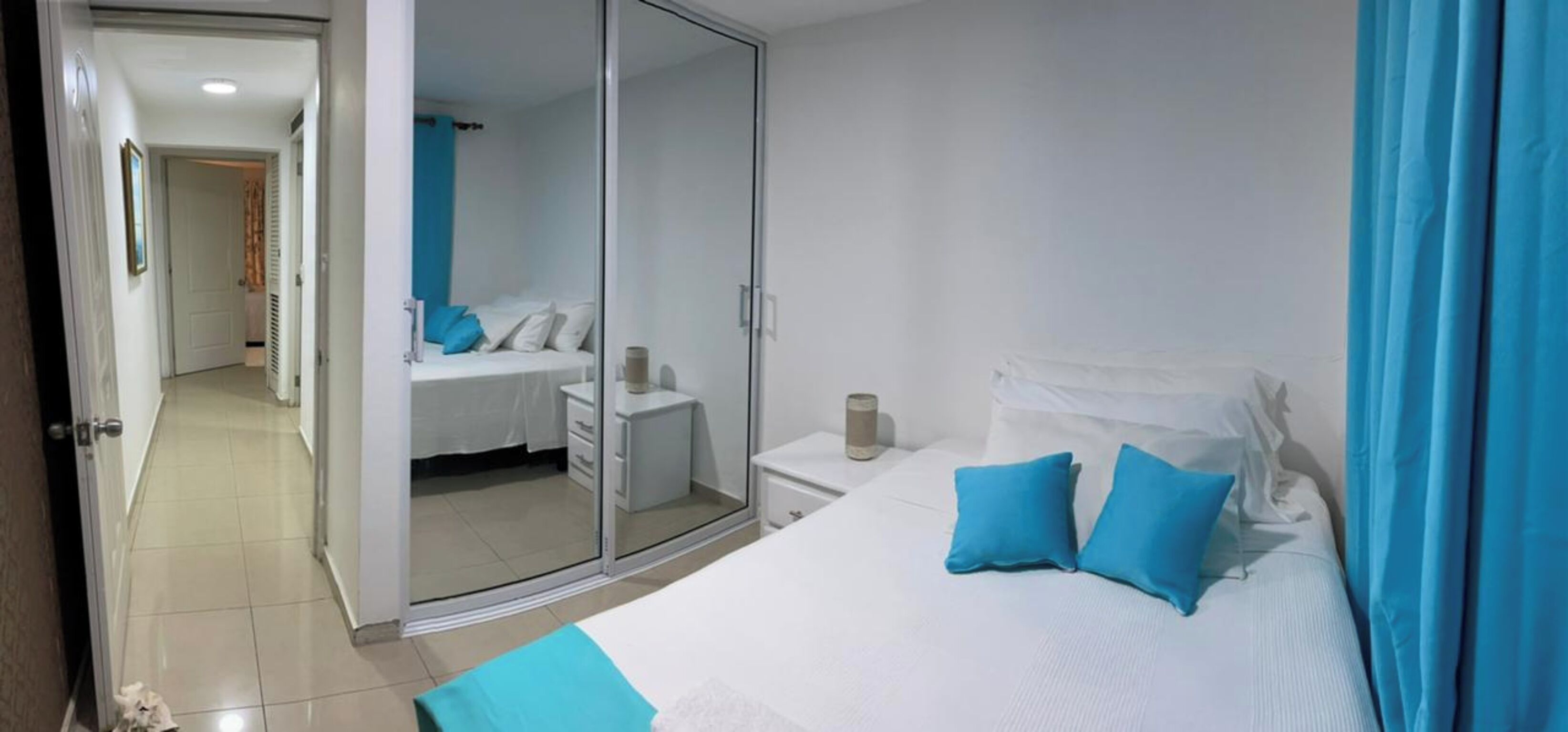 Un dormitorio con cama, mesita de noche, espejo y una puerta corrediza que da a otra habitación.