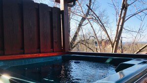 A hot tub with a wooden deck and a view of leafless trees.