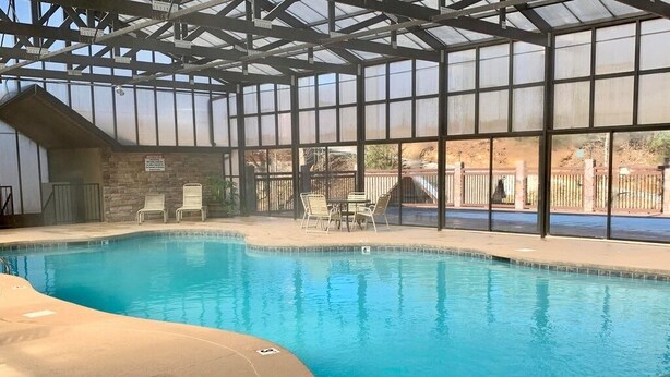 An indoor swimming pool with clear glass walls, a concrete deck, and a few lounge chairs.