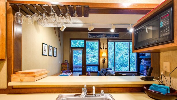 A kitchen with a large island, wooden cabinetry, a built-in microwave, and a view of the outdoors through large windows.