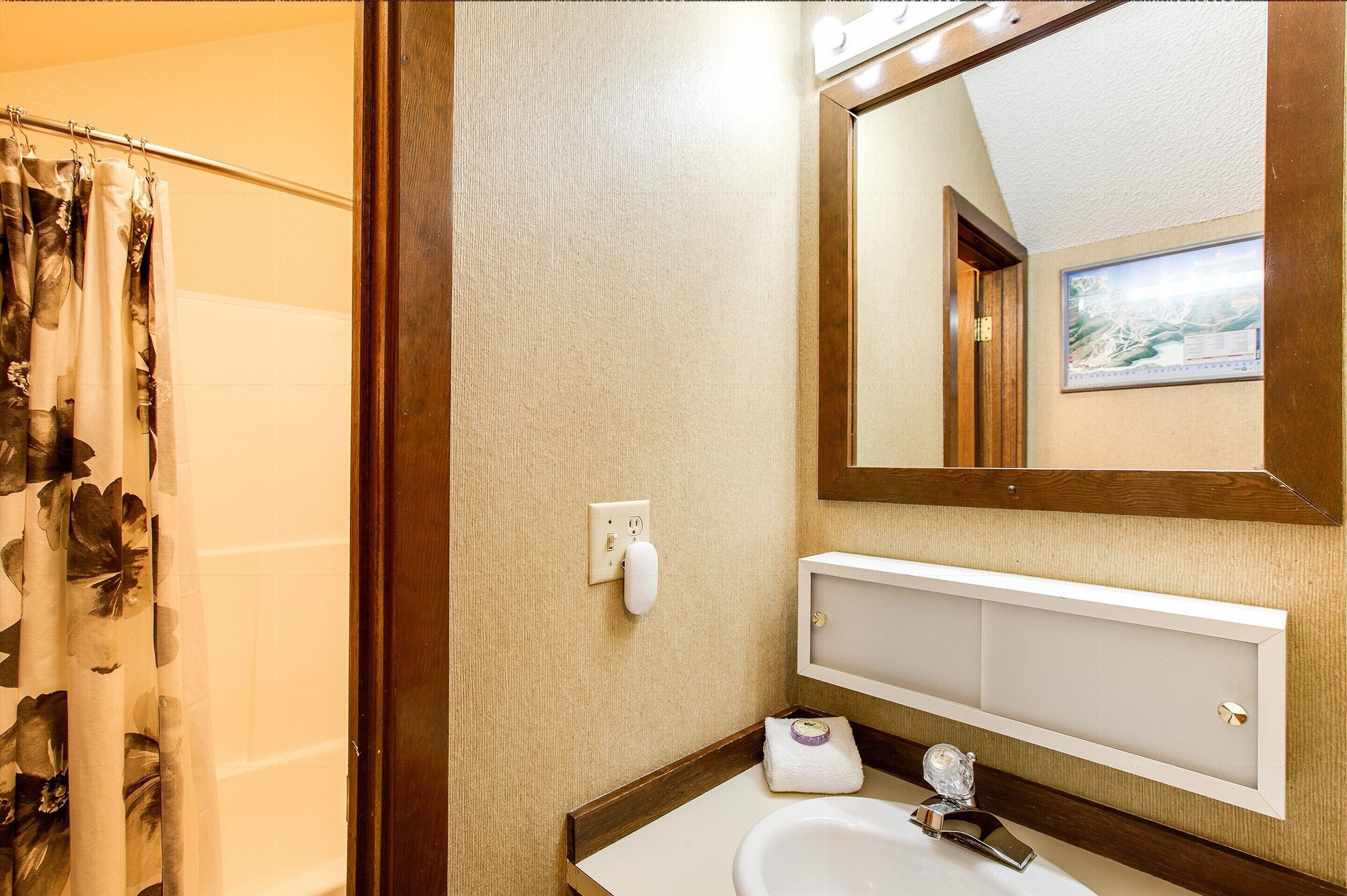 Un baño con cortina de ducha, lavamanos, espejo y toallero.