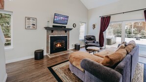 Una sala de estar con chimenea, televisor, sofá y vistas al exterior.
