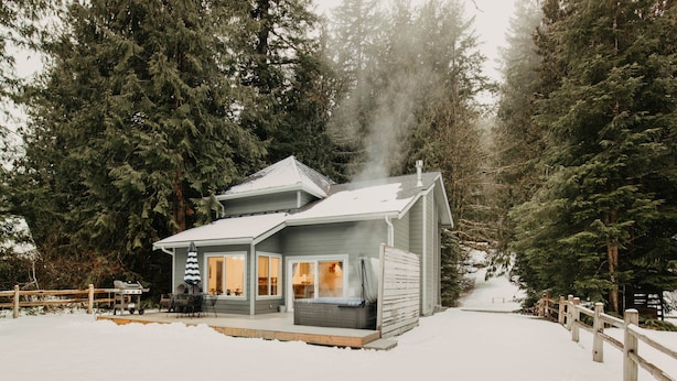 Una cabaña con jacuzzi, rodeada de nieve y altos árboles.