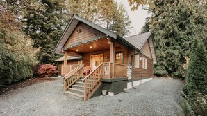 A wooden cabin with a porch, steps, and a gravel driveway surrounded by trees. - 65gs - Hot Tub - Wi-fi - Pets Ok - Bbq (Deming)