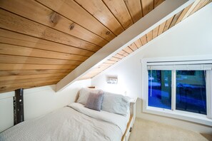 A bedroom with a sloped ceiling, a bed with a patterned bedspread, a nightstand, and a window with a view of trees. - Snowline Cabin 66 - Hot Tub - Wi-fi - 3 Bedroom - Sleeps 10 (Deming)