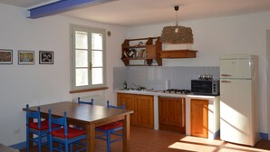 A kitchen with a dining table, chairs, a refrigerator, a stove, and a hanging light fixture. - Girasole - Cozy, bright vacation apartment with pool, large garden near the sea (Castiglione della Pescaia)