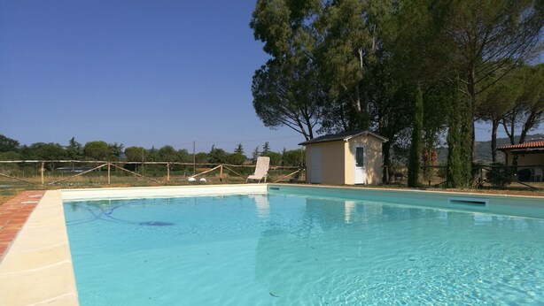A clear swimming pool with a small adjacent building, surrounded by trees and a fenced area. - Girasole - Cozy, bright vacation apartment with pool, large garden near the sea (Castiglione della Pescaia)