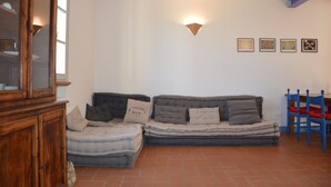 A living room with a sofa, a wooden cabinet, and a blue chair. - Girasole - Cozy, bright vacation apartment with pool, large garden near the sea (Castiglione della Pescaia)