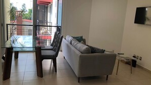 Ein Wohnzimmer mit einer Couch, einem Glastisch und einem an der Wand befestigten Fernseher.