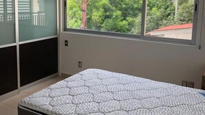 Ein Schlafzimmer mit einem Bett, einem Fenster und Blick auf Grünfläche.