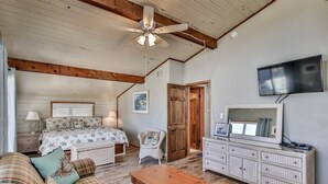 Une chambre confortable avec un lit, un ventilateur de plafond en bois, une télévision et une commode.
