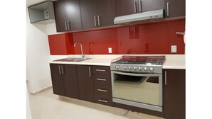 Une cuisine avec des meubles de couleur sombre, un crédence rouge, une cuisinière à gaz et un four encastré.
