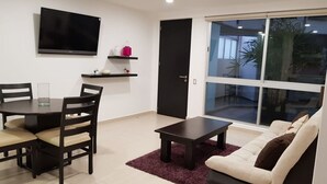 Un salon moderne comprenant un canapé, une table basse, un téléviseur fixé au mur et un coin repas avec des chaises et une table.