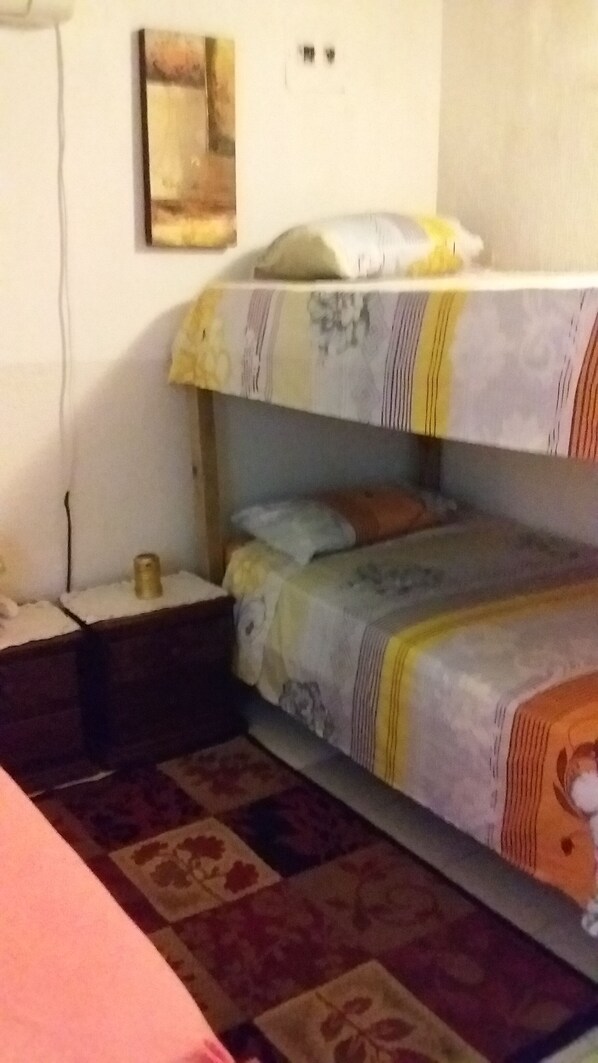 A bunk bed room with a patterned rug, a small bedside table, and a wall-mounted light fixture.