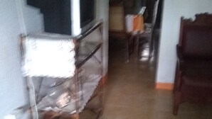 Quarto com televisão em uma estante, uma cadeira e uma mesa com uma revista.