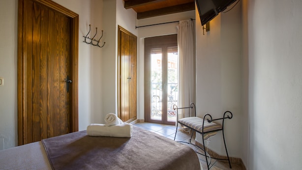 A bedroom with a bed, a wooden door, a window with curtains, and a television mounted on the wall. - Hostal Valle del Sol Confort Rooms (Álora)