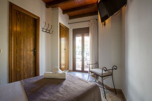 Een slaapkamer met een bed, een houten deur, een raam met gordijnen en een aan de muur bevestigde televisie.