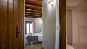 A hotel room with a wooden door, a bed with a white headboard, a bathroom with a toilet and shower, and a window with curtains. - Hostal Valle del Sol Confort Rooms (Álora)
