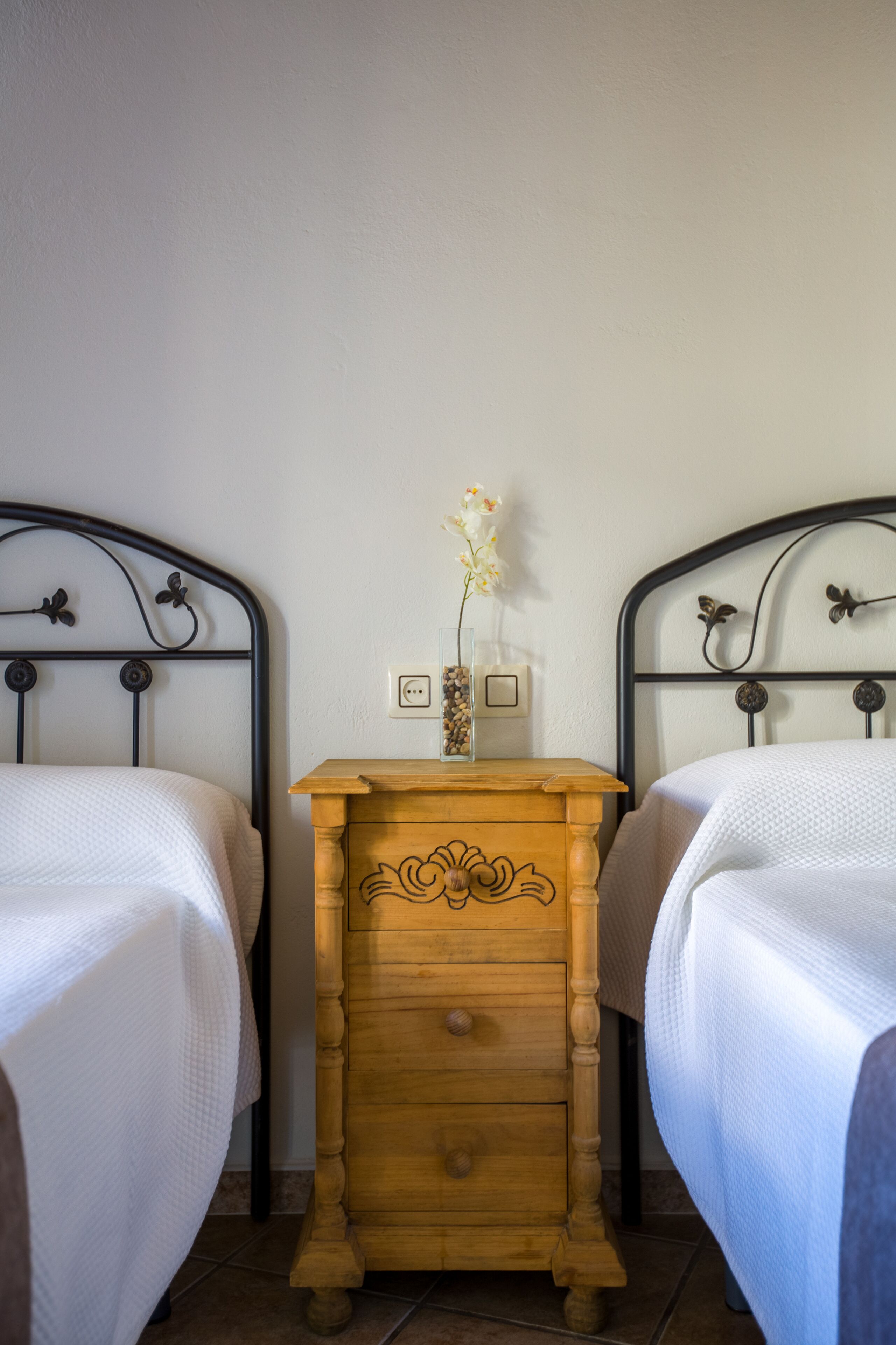 Un dormitorio con dos camas, un aparador de madera y una mesita de noche con un florero.