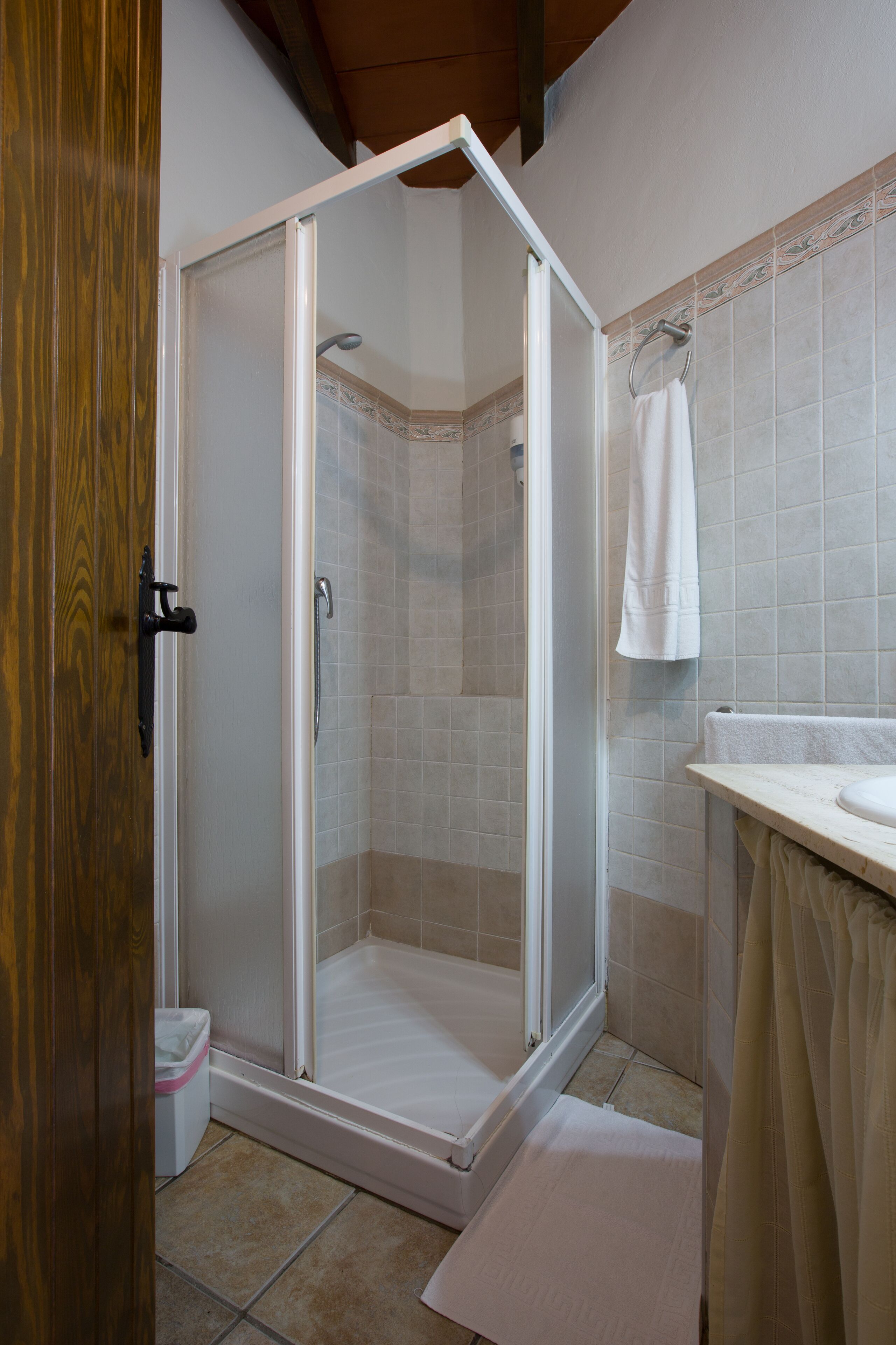 A shower with a glass door, a white sink, and a towel hanging on the wall.