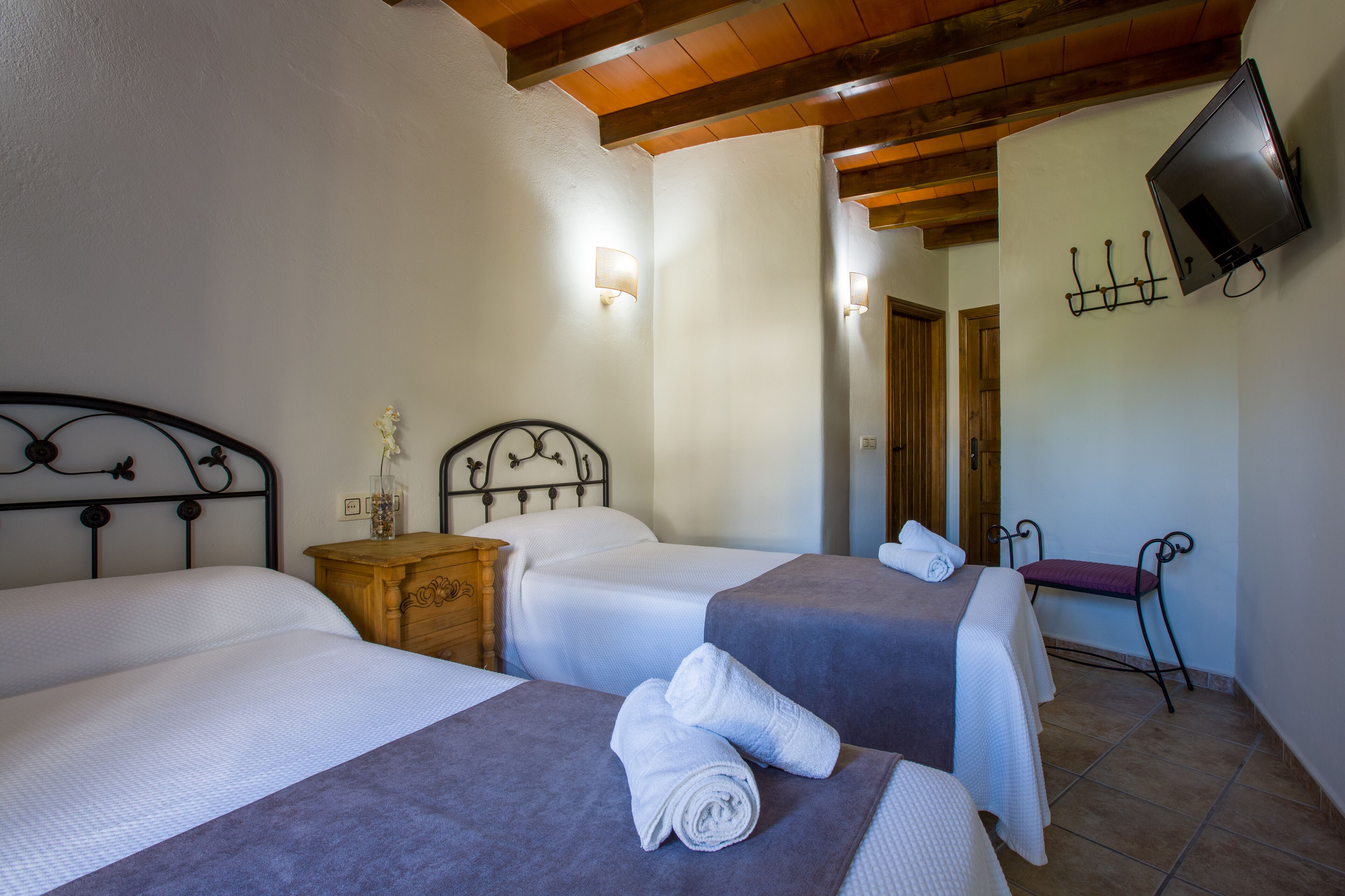 Habitación de hotel con dos camas, una mesita de noche de madera, un televisor montado en la pared y un espejo que refleja la habitación.