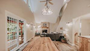 A spacious living area with a large wooden dining table, a fireplace, and a view of the outdoors.