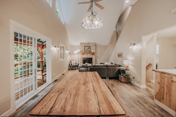 A spacious living area with a large wooden dining table, a fireplace, and a view of the outdoors.