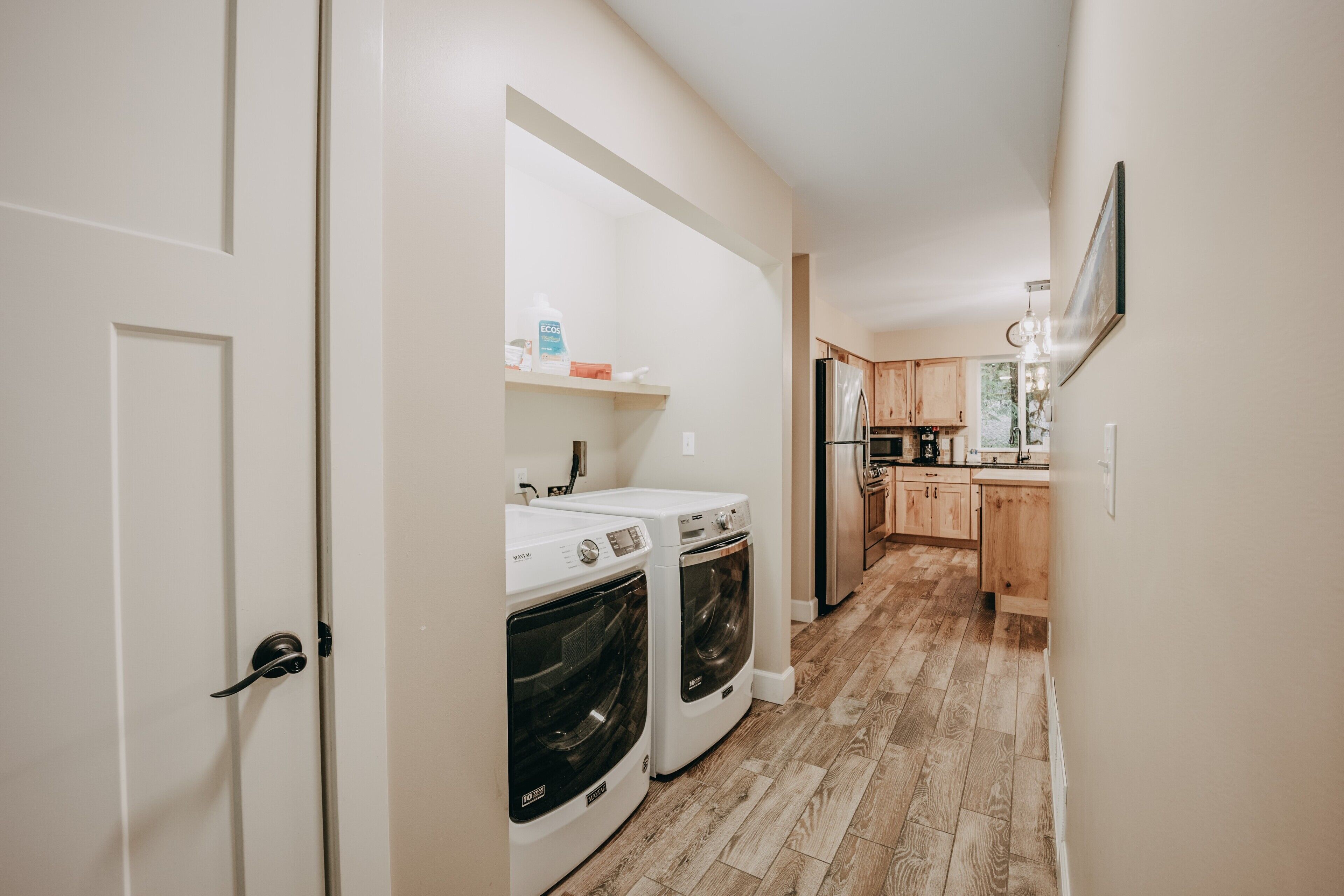 A laundry room with two front-loading washers and dryers, wooden cabinets, and a kitchen area with a refrigerator and wooden cabinets.