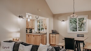 A modern living room with a gray sofa, a wooden dining table, and a kitchen in the background.