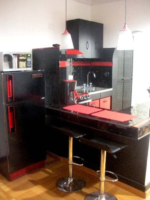 Une cuisine de taille réduite avec un plan de travail noir, des touches de couleur rouge et un four à micro-ondes.