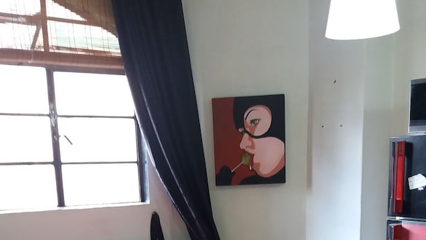 A living room with a sofa, a small table, a painting on the wall, and a window with curtains. - Universidad Javeriana Cll 41 (Bogotá)