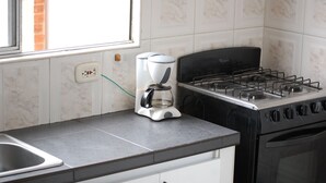 Una cocina con estufa a gas, cafetera y lavadero.