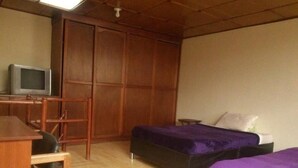 A room with a wooden desk, a television, a bed with purple bedding, and a yellow chair.