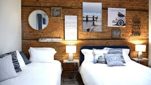 A hotel room with two beds, a brick wall, and various decorative items including a mirror, framed pictures, and pillows with text. - Best Spot in Town! Sunny Terrace - 3 bedrooms w/ private bathrooms - Fast WI-FI  (Montreal)