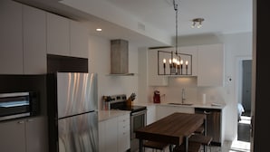 A modern kitchen with stainless steel appliances, a wooden dining table, and a pendant light. - Best Spot in Town! Sunny Terrace - 3 bedrooms w/ private bathrooms - Fast WI-FI  (Montreal)