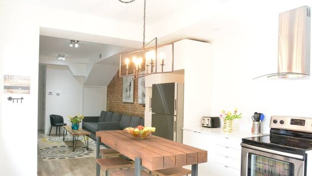 A modern kitchen with a wooden table, bar stools, a built-in oven, and a hanging light fixture. - Best Spot in Town! Sunny Terrace - 3 bedrooms w/ private bathrooms - Fast WI-FI  (Montreal)