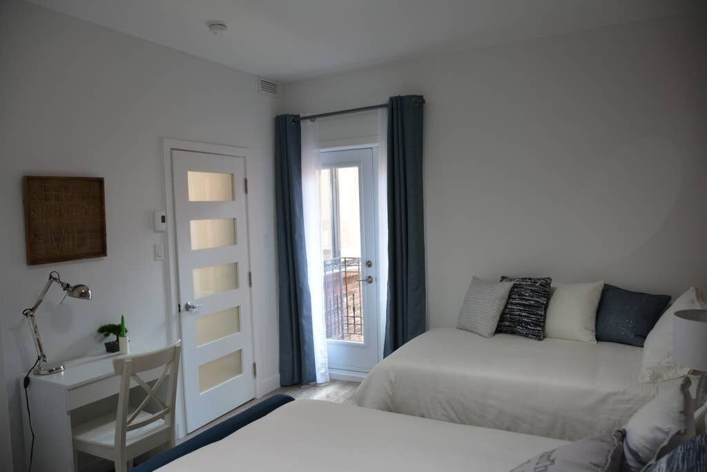 A bedroom with two beds, a desk, a chair, and a door leading to a balcony.