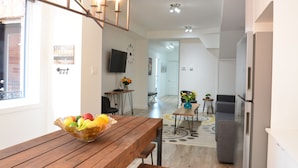A modern kitchen with a wooden dining table, a fruit bowl, and a refrigerator. - Best Spot in Town! Sunny Terrace - 3 bedrooms w/ private bathrooms - Fast WI-FI  (Montreal)